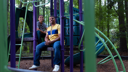 A child poses with his father on a purple and green jungle gym.