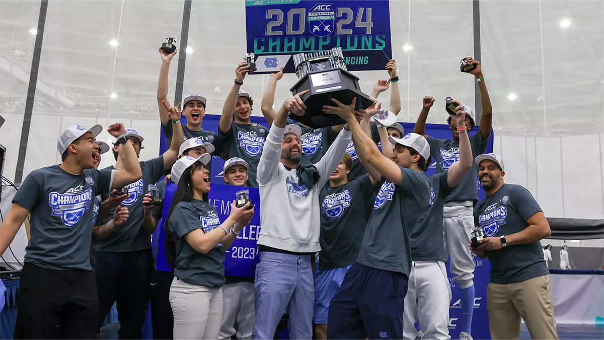 The Carolina men's fencing team celebrating as a group and lifting a trophy after winning the conference championship.