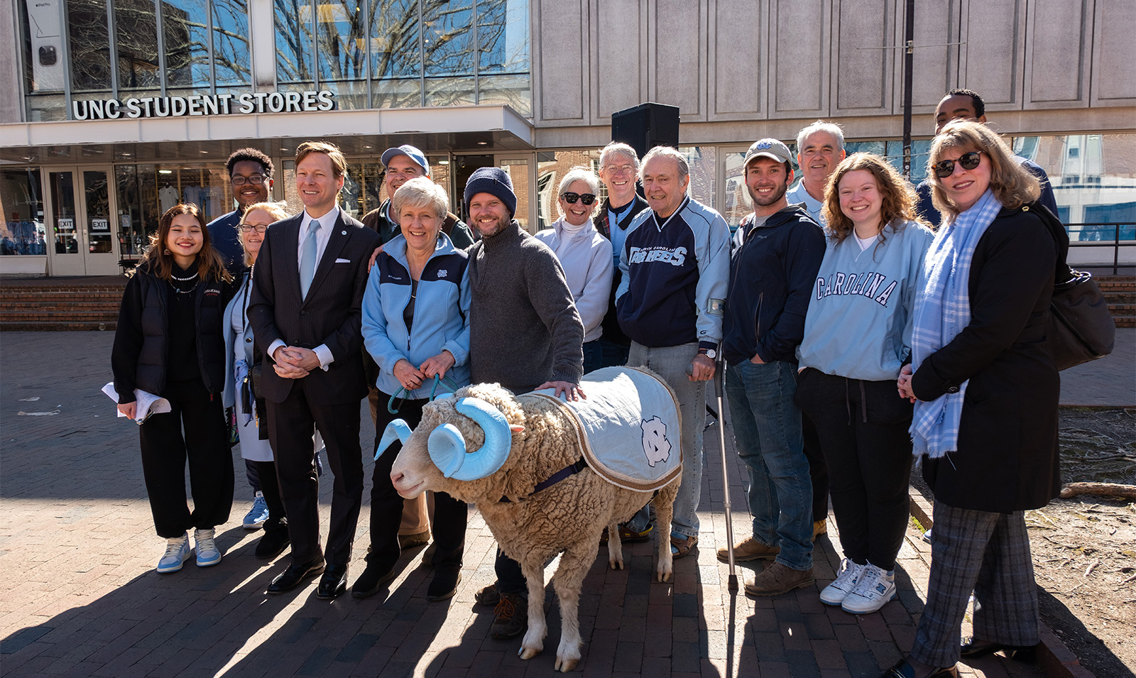 A group of people posing with a live ram mascot, Rameses, on the campus of UNC-Chapel Hill.