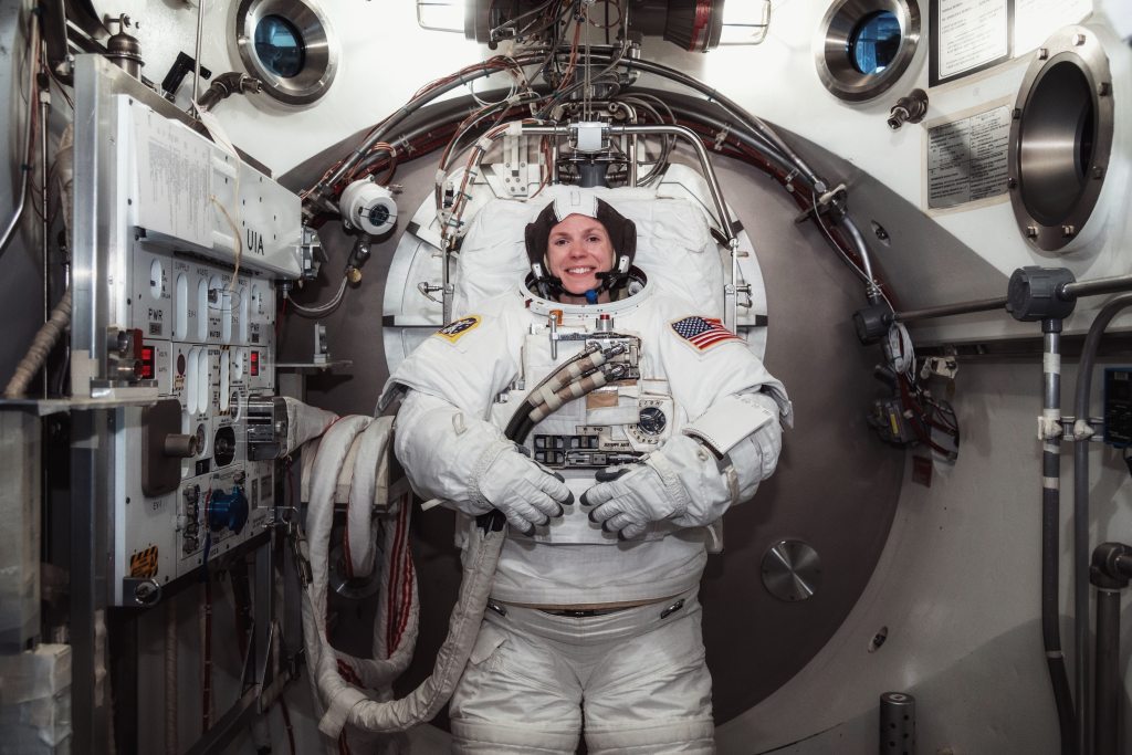 Zelda Cardman smiling in her spacesuit surrounded by NASA tech.